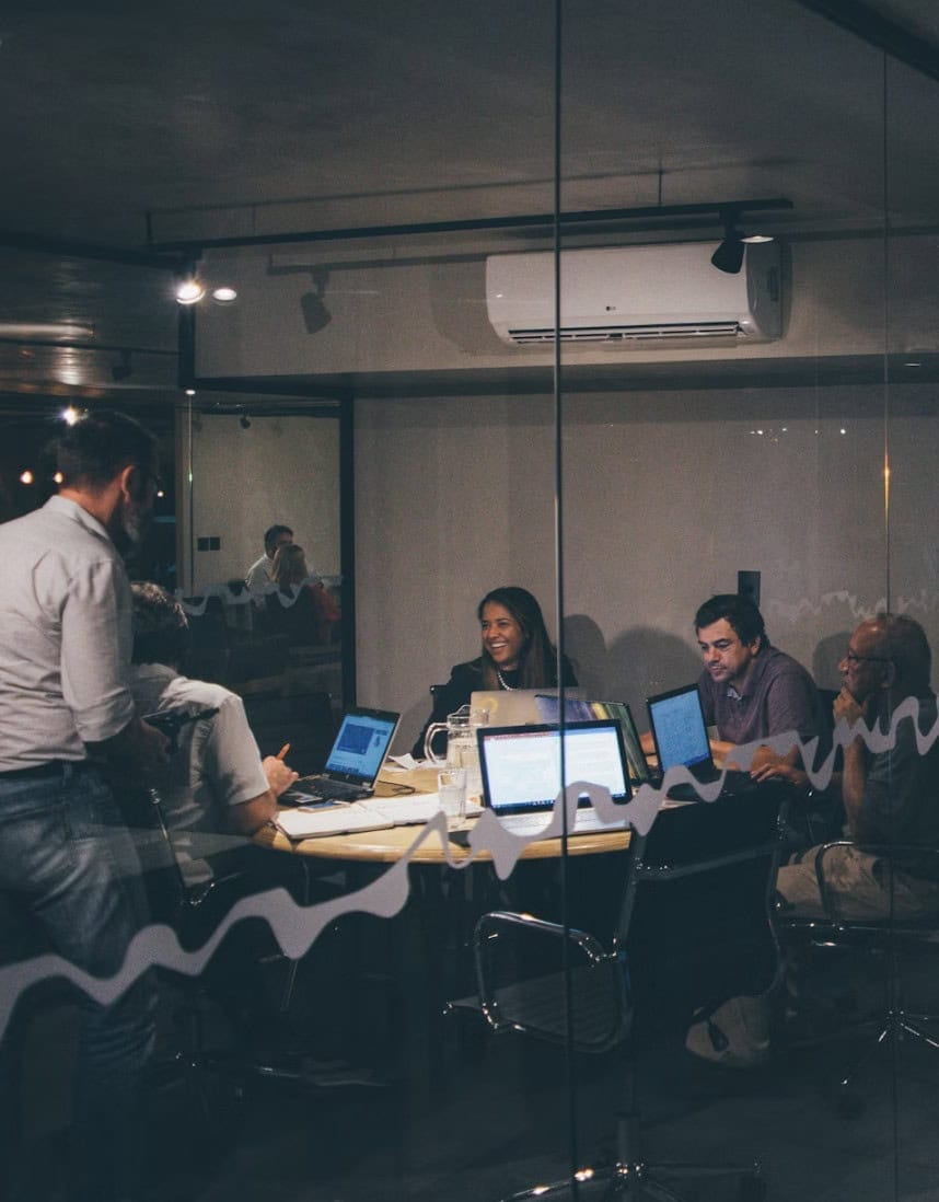 Screenshot 2025-09-29 at 12.42.46 PM Collaboration meeting with professionals using laptops in a modern conference room.