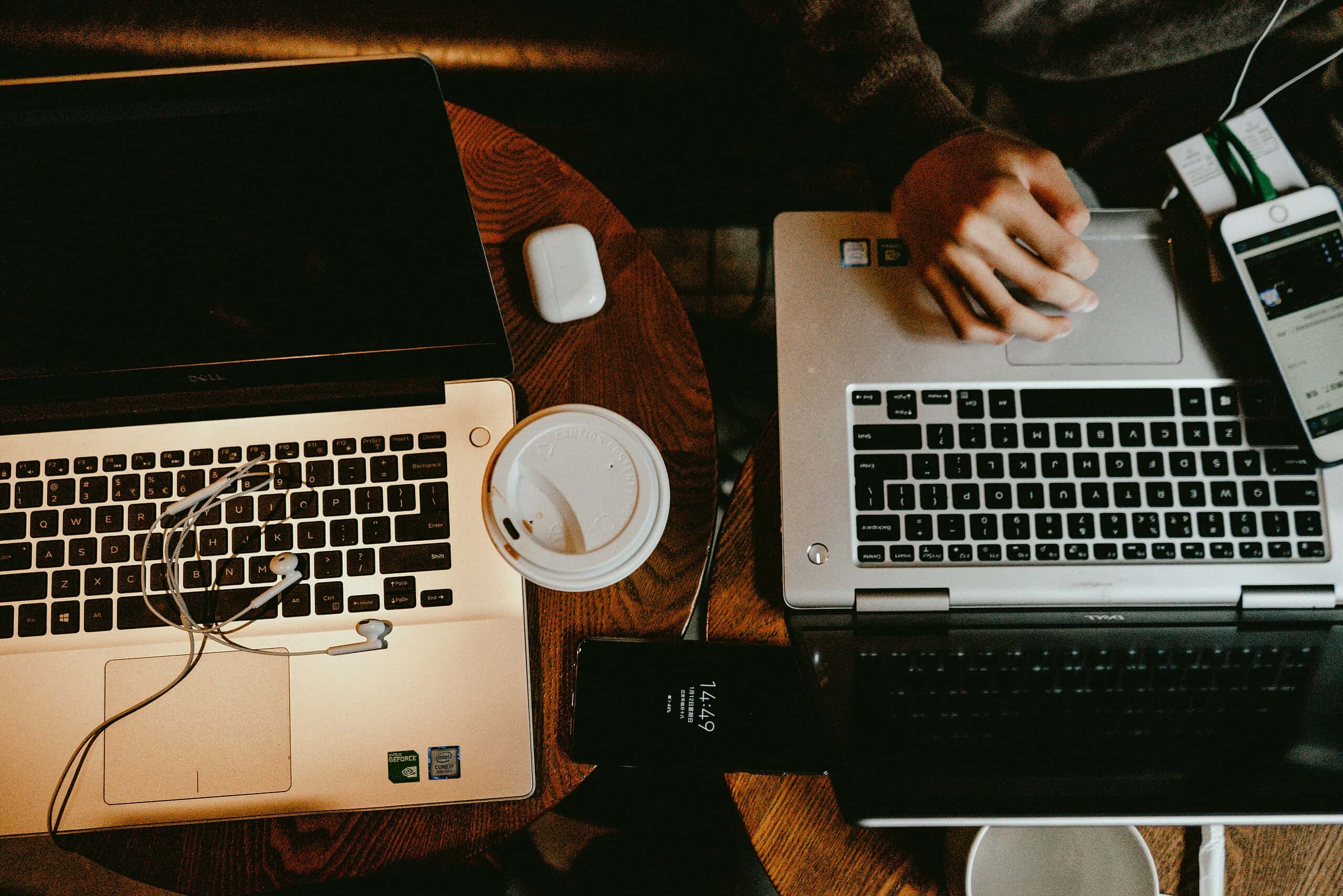 Laptop computers working on a wooden desk with coffee, wireless earbuds, and smartphone, representing tech, remote work, and digital communication.