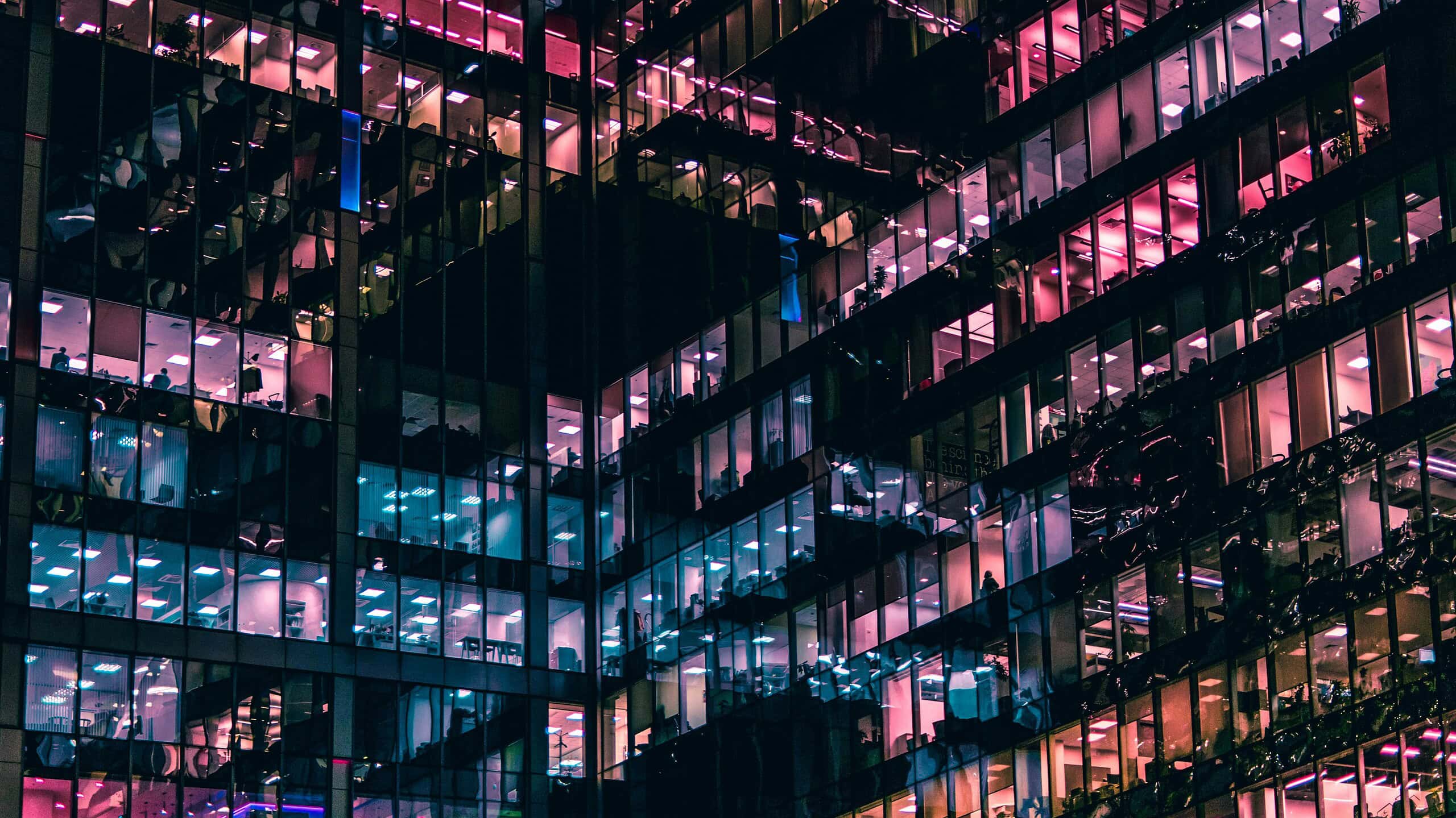Office building illuminated with vibrant pink and blue neon lights at night.