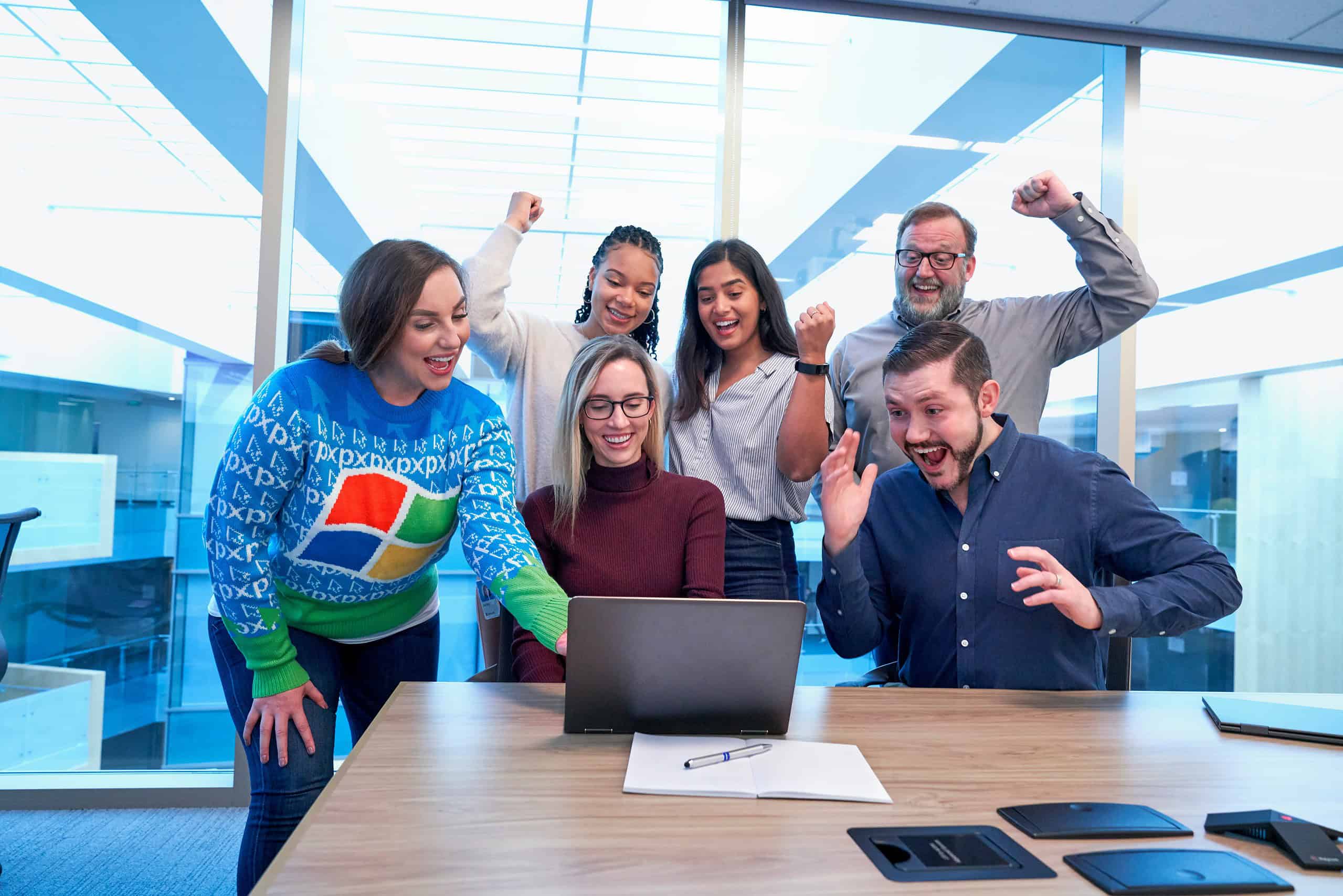 Happy diverse team celebrating success around laptop in modern office, teamwork, tech innovation, collaboration, achievement, positive work environment.